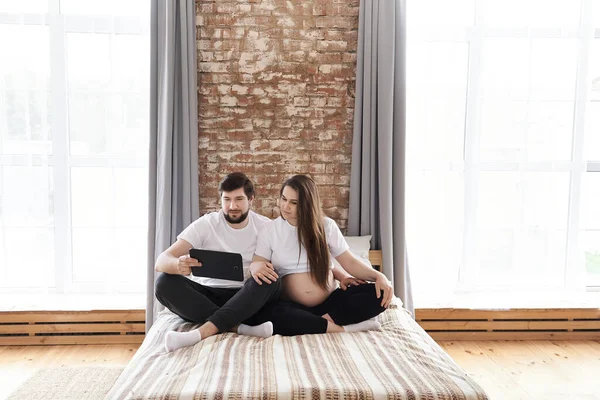 年轻男子和他怀孕的妻子在家里的沙发上使用平板电脑 母性和亲子关系 幸福的家庭观念 复制空间 互联网 现代技术 在一起 — 图库照片