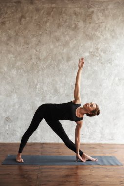 Yoga yapan güçlü orta yaşlı kadın Utthita Trikonasana pozu, genişletilmiş üçgen egzersizi, evde ya da yoga stüdyosunda dikey egzersiz. Sağlıklı yaşam tarzı kavramı. Boşluğu kopyala