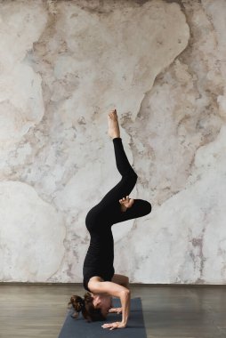 Yoga yapan güçlü bir kadın, amuda kalkarak poz veren, içeride çalışan, siyah spor giyimli, kenar manzaralı, tam boy, dikey. Sağlıklı, uyumlu ve yaşam konsepti dengeli. Reklam alanı