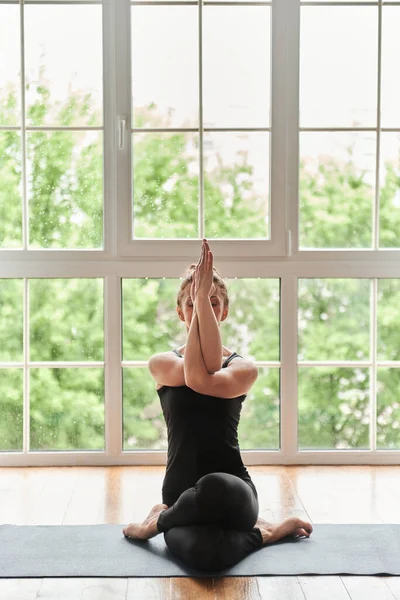 Yogi中年女性练习瑜伽 坐着做瑜伽练习 以代替Gomukasana练习 奶牛脸在家里摆姿势或在有大窗户的瑜伽工作室摆姿势 专心和健康的生活方式概念 — 图库照片