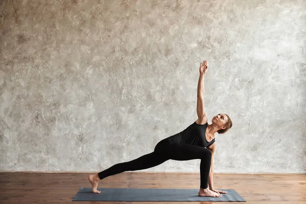 一个女人练习瑜伽 做各种不同的Utthita Parsvakonasana运动 伸展侧角的姿势 抬起头来 穿着黑色运动服 室内全长 健康生活的概念 广告空间 — 图库照片