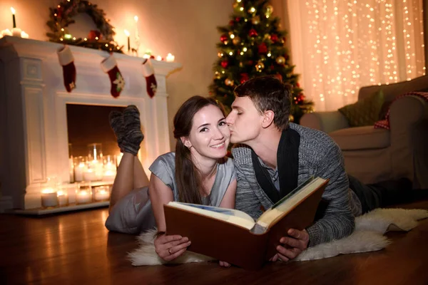 A gentle kiss of a family spouses while looking through some photos, the wife is very happy. Cheerful couple in love reading the book during the Christmas vacation.