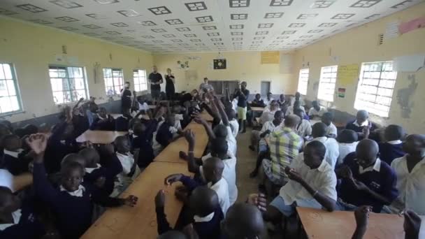 KISUMU, KENYA - 15 MAGGIO 2018: Un grande gruppo di bambini e adolescenti africani seduti, volontari caucasici aiutano a fare braccialetti — Video Stock