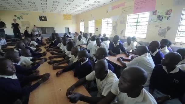 Kisumu, Kenya - 15 maj 2018: Stora grupp av skallig afrikanska barn och ungdomar sitter och lyssnar till kaukasiska frivilliga. — Stockvideo
