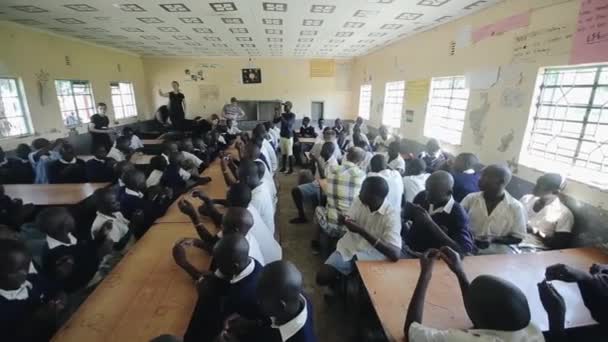 КИСУМУ, КЕНЯ - 15 мая 2018 года: Кавказские добровольцы и африканские дети, подростки в форме, сидящие вместе в классе . — стоковое видео