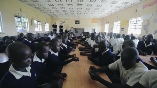 KISUMU, KENIA - 15 DE MAYO DE 2018: Grupo de niños y adolescentes africanos en uniforme sentados en el patio trasero de la escuela y mirando a alguien. Multitud de alumnos disfrutando del día de verano en el pueblo de África . — Vídeos de Stock