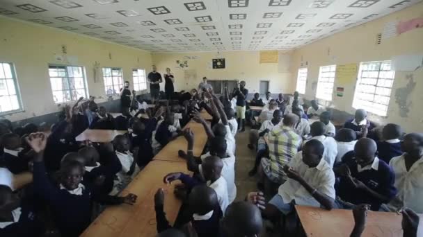 KISUMU, KENYA - 15 MAGGIO 2018: Gruppo di bambini e adolescenti africani seduti, volontari caucasici che aiutano a fare braccialetti . — Video Stock