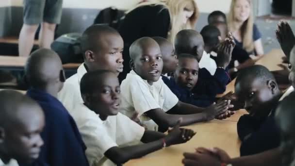 Kisumu, Kenya - 15 maj 2018: Grupp skallig afrikanska barn sitter. Pojkar och flickor i uniform sjunga och klappa händerna. — Stockvideo