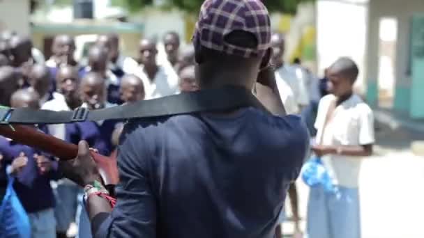 Kisumu, Kenia - mei 15, 2018: Jonge man met gitaar zingen aan groep Afrikaanse kinderen in uniform. Kinderen in de buurt van schoolgebouw — Stockvideo