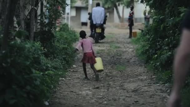 KISUMU, KENYA - 17 Mei 2018: Pemandangan kembali gadis afrika yang membawa tabung berisi air. anak berjalan melalui jalan desa . — Stok Video