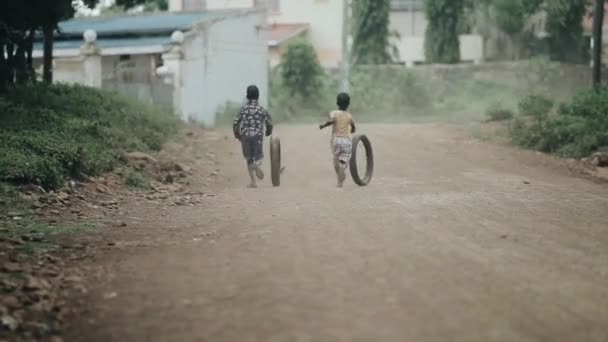 Kisumu, Kenia - 17 maja 2018: Widok z tyłu dwóch chłopców Afryki uruchomione poprzez droga i gry z samochodów opon w miejscowości. — Wideo stockowe