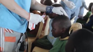 Kisumu, Kenya - 19 Mayıs 2018: Beyaz adam tıbbi merhem ile kafa Afrikalı çocuklar yaralar çizim eldiven.