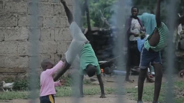 KENYA, KISUMU, 15.05.2018. View through fence. African children walking in house yard. Boys doing gymnastic exercises. — Stock Video