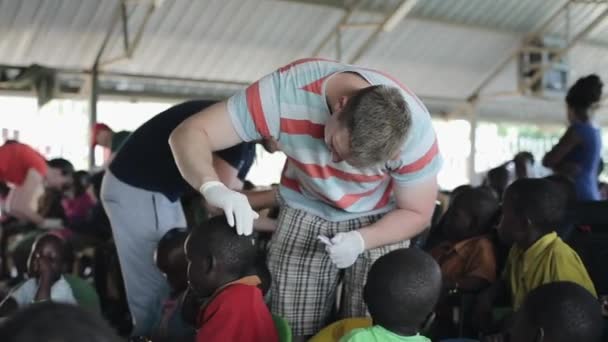 KISUMU, KENYA - 19 de maio de 2018: voluntários caucasianos ajudando na escola na África. Homem tratando feridas na cabeça com salve . — Vídeo de Stock