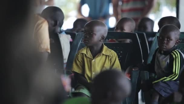 КИСУМУ, КЕНЯ - 19 мая 2018 года: Группа маленьких африканских детей, сидящих в школе снаружи и серьезно смотрящих прямо . — стоковое видео