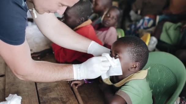 KISUMU,KENYA - MAY 19, 2018:Caucasian man in gloves helping to african children. Kids are blow out their snots in napkin. — Stock Video