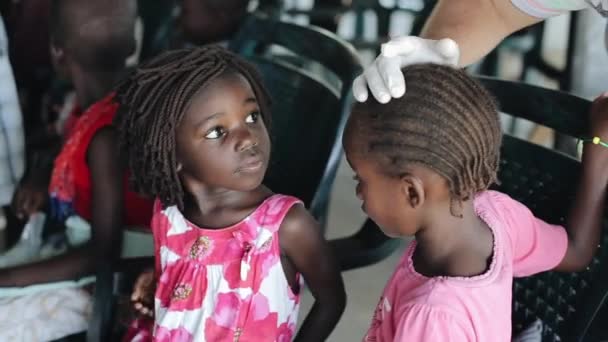 Kisumu, Kenya - 19 maj 2018:Caucasian volontärer hjälpa i skola i Afrika. Man behandla sår på huvudet av flickor med salve. — Stockvideo