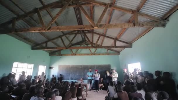 КИСУМУ, КЕНЯ - 21 мая 2018 года: Камера движется вниз. Кавказские добровольцы говорят в школе в Африке. Дети сидят в классе . — стоковое видео
