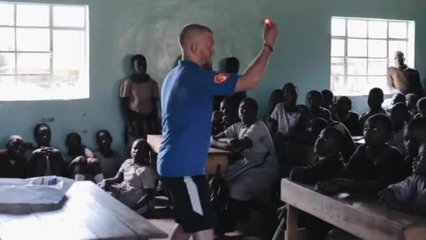 Kisumu, Kenya - 21 Mayıs 2018: Beyaz adam hileler ampul ile küçük Afrika okulda çocuklar, kalabalık için gösterir — Stok video