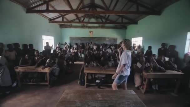 KISUMU, KENYA - 21 de maio de 2018: Mulher caucasiana, voluntária vem para a sala de aula na escola africana. Meninos e meninas sentam-se na mesa . — Vídeo de Stock