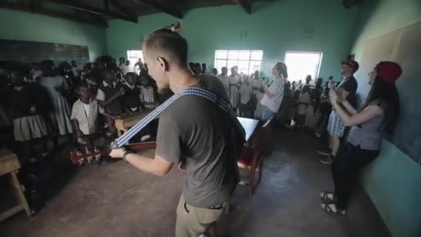 Kisumu, kenia - 21. Mai 2018: Gruppe afrikanischer Kinder singt und tanzt im Klassenzimmer mit kaukasischen Freiwilligen mit Gitarre. — Stockvideo