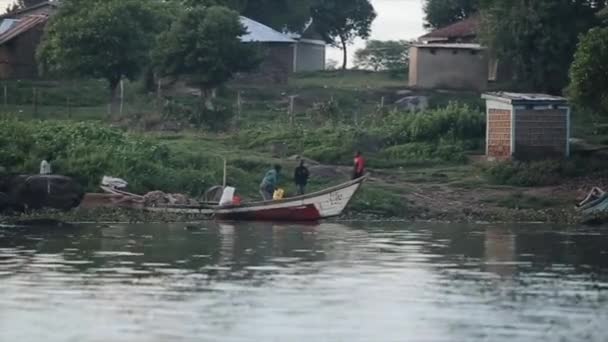 Kisumu, Kenya - 2018. május 21.: Nézd a csónakot a faluba, a folyó partján. Csoport afrikaiak férfiak megy a halászatot folytató hajó. — Stock videók