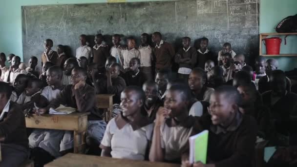 KISUMU, KENYA - 21 MAI 2018: Vedere a sălii mari de clasă plină de copii africani. Băieții și fetele zâmbesc și se ridică . — Videoclip de stoc