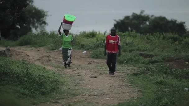 KISUMU, KENYA - 23 Mei 2018: Wanita Afrika berjalan melalui jalan desa, membawa mangkuk di atas kepalanya. Man pergi di dekatnya . — Stok Video