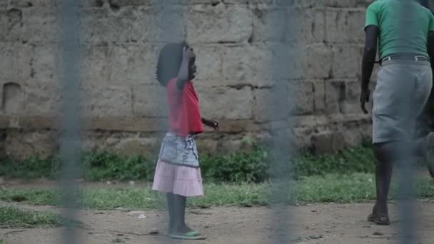 Kisumu, Kenya - 23 Mayıs 2018: Çitin üzerinden görünümü. Grup dışında vakit Afrika insan. Küçük kız eğleniyor. — Stok video