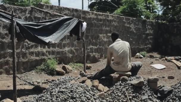Vista posterior del hombre de África trabaja en el sitio de construcción. Guy está sentado en la cantera. — Vídeo de stock