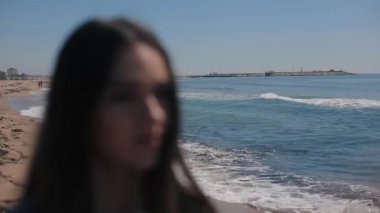 Plaj ve deniz doğal görünümünü açık güneşli bir kızla bulanık bir portresi. Kız güneş gözlüğü üzerinde koyar. Odak arka plandan kıza geçer. Deniz dalgaları yansıması perdeleri