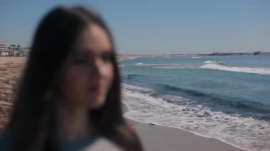 Denizin dalgaları sıçramasına ile manzarayı uzun saçlı bir kız bulanık bir close-up. Güneş gözlüğü üzerinde koyarak ve gülümseyen kadın. Arka plandan kişiye değişen odak. Deniz