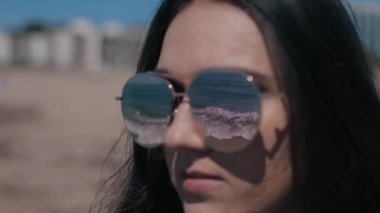 Güzel bir kız sahilde güneş gözlüğü yakın çekim portresi. Denizin dalgaları ile yansıtmak içinde güneş gözlüğü