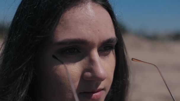 Una vista cercana de una hermosa chica poniéndose gafas de sol. Las olas del mar se reflejan en las sombras — Vídeo de stock