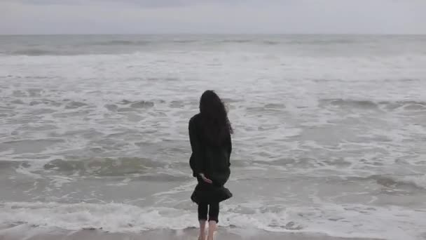 Egy gyönyörű mezítláb lány meleg ruhákat fut a tenger felé, egy hideg napon, lesz, hogy félek a hideg víz, és fut vissza — Stock videók
