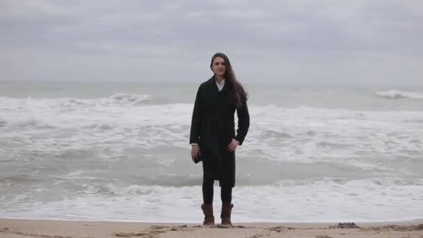 Uma menina bonita de pé na praia em um dia de vento frio — Vídeo de Stock