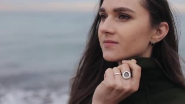 Yakın çekim yeşil paltolu sahil tarafında isteyen güzel bir gülümseyen kız. Arka plan bulanık. Doğa için değişen odak. Sabah deniz