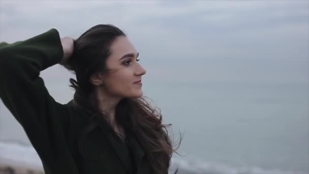 Achteraanzicht van een mooi meisje in lederen laarzen en een groene lange jas lopen op het strand — Stockvideo