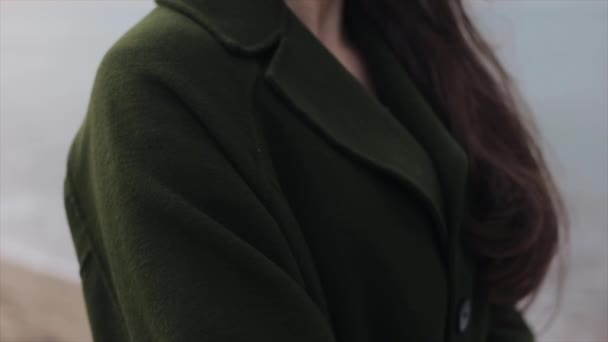 Близкий вид женского плеча и груди в теплом пальто на размытом морском фоне. Девушка положила левую руку на правое плечо — стоковое видео
