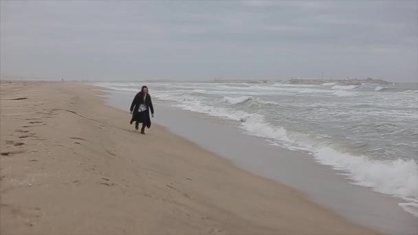Красивая девушка бежит по песчаному пляжу в прохладный весенний день — стоковое видео