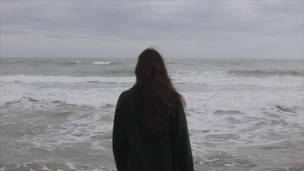 Dos vue demi-corps d'une belle fille aux longs cheveux foncés vêtue d'un manteau vert foncé en laine profitant de la vue sur la mer — Video