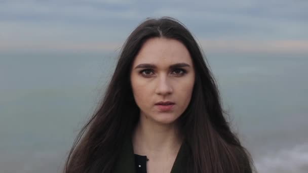 Um retrato de close-up de uma menina bonita com longos cabelos escuros soltos contra o mar borrado e fundo do céu — Vídeo de Stock