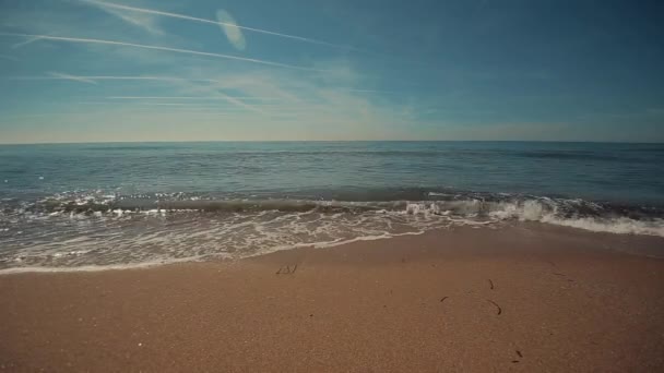 Nyugodt tenger néhány hullámok feltörése a homokos strandtól. Az egyes pályák, a repülőgépek, a háttérben a nyári ég — Stock videók