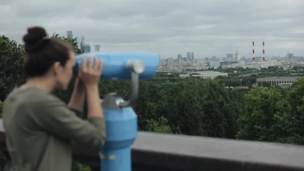 Вид сбоку красивой девушки, наблюдающей за городом через туристический телескоп — стоковое видео