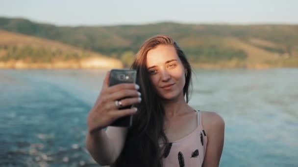 Piękna dziewczyna co selfie z jej telefon stojąc z przodu z rzeki i góry. Portret połowy ciała — Wideo stockowe