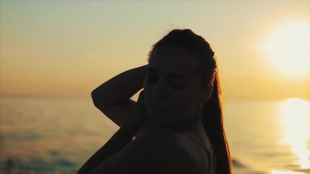 En vacker flicka poserar tittar ner och röra vid sitt långa hår. Solnedgång över floden i bakgrunden. Stäng upp sida stående — Stockvideo