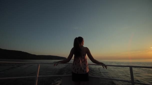 A beautiful girl stands in the wind against sunset sky, river, and mountains. Back view — Stock Video