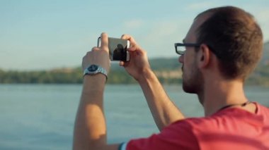 Bir close-up genç bir çocuk onun iPhone su içinde belgili tanımlık geçmiş Dağları ile fotoğraf çekme. Odak doğadan adama geçer.