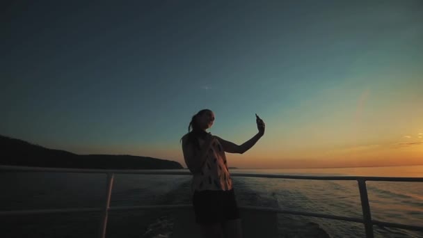 Una hermosa chica seductora está posando y haciendo selfie con la puesta de sol sobre el río en el fondo — Vídeos de Stock