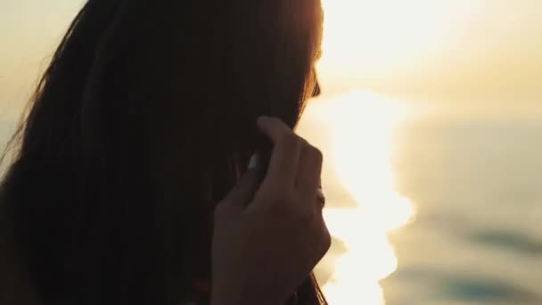 Un primo piano di una bella ragazza che gioca con lunghi capelli castani sciolti con il tramonto e l'acqua sullo sfondo — Video Stock